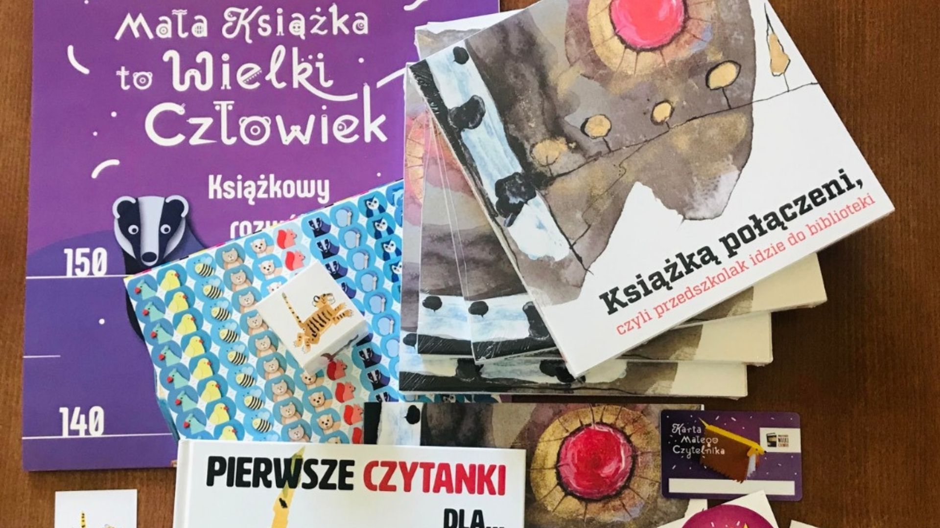 Zdjęcie przedstawia części składowe wyprawki czytelniczej dla przedszkolaka - książki i gadżety dla dziecka oraz broszurę informacyjną dla rodziców.